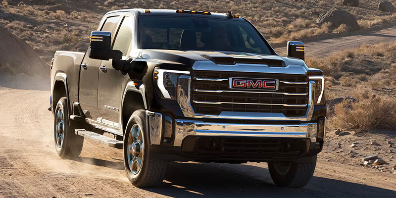 a black 2025 GMC 3500HD driving down a dirt road