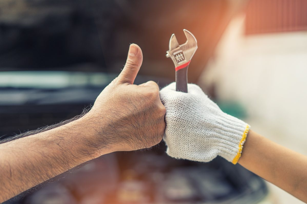 a hand giving a fist bump while giving a thumbs up and the other hand holding a wrench